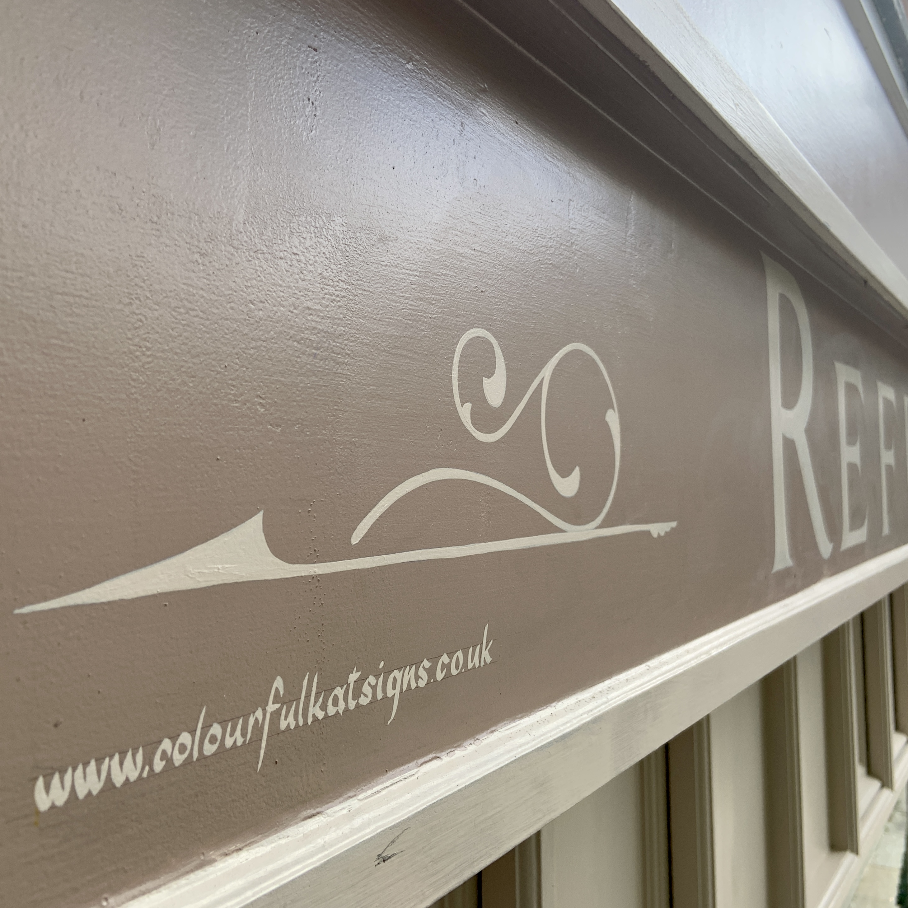 close up detail of SCROLL and signwork in cream on almond colour shop fascia