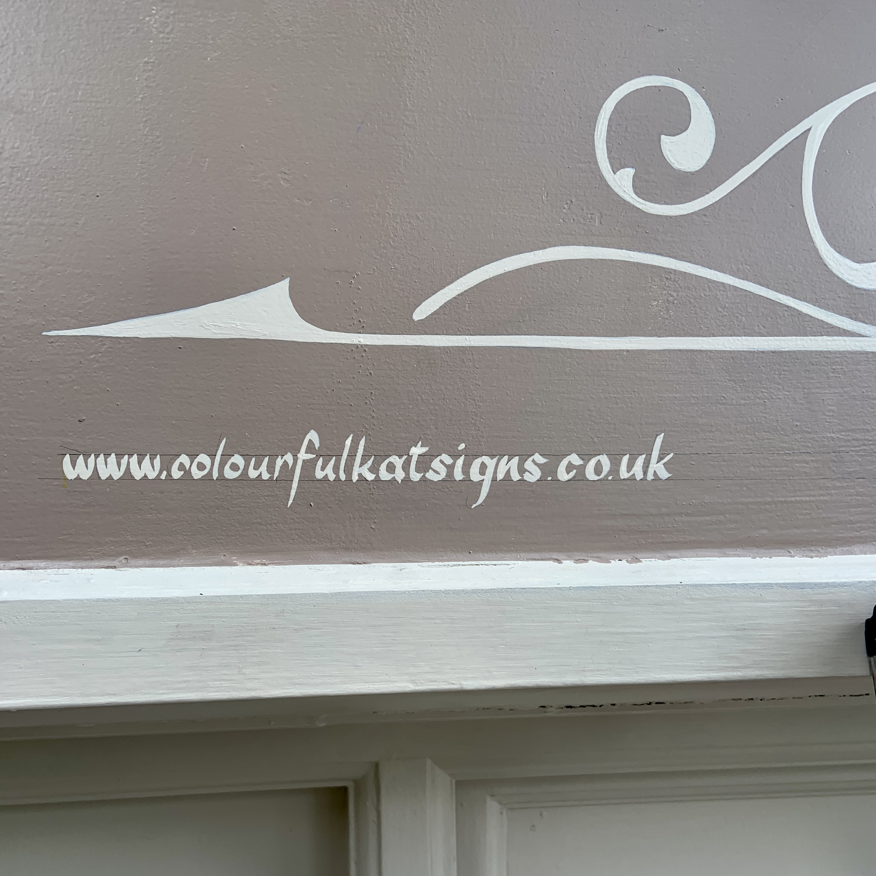 Close up detail of Scroll and signwork in cream on almond colour shop fascia